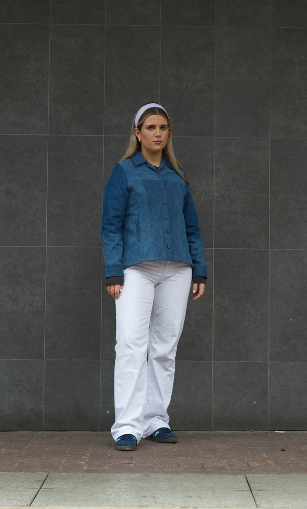 The 60s model posing face on in front of a grey tiled wall.