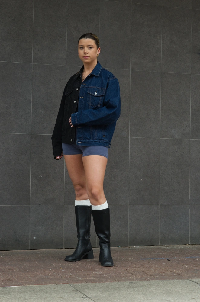 The 80s model posed looking down towards the audience, standing in front of a grey tiled wall.