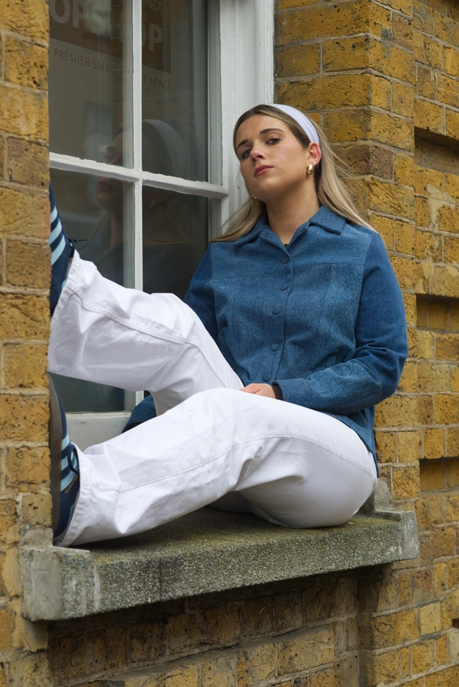 The 60s model posed, sitting on a window ledge facing towards the audience.